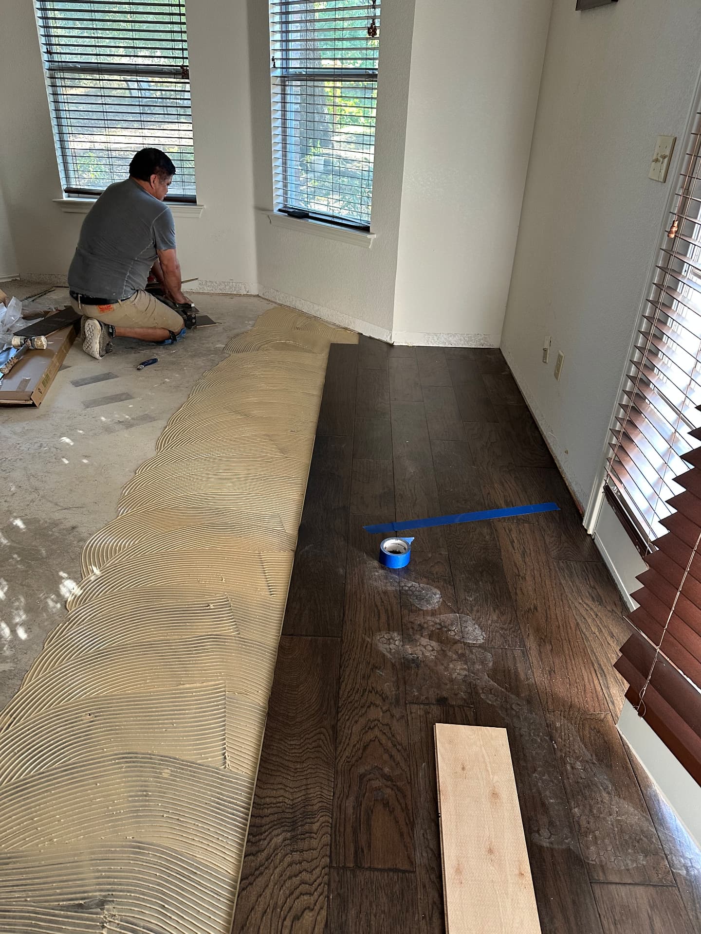 Crew laying dark engineered hardwood over a glued concrete subfloor in a sunlit room