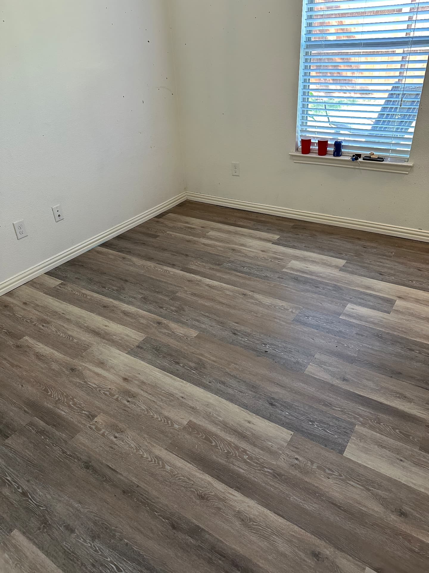 Gray and taupe wood-look vinyl plank flooring in an empty bedroom with window light