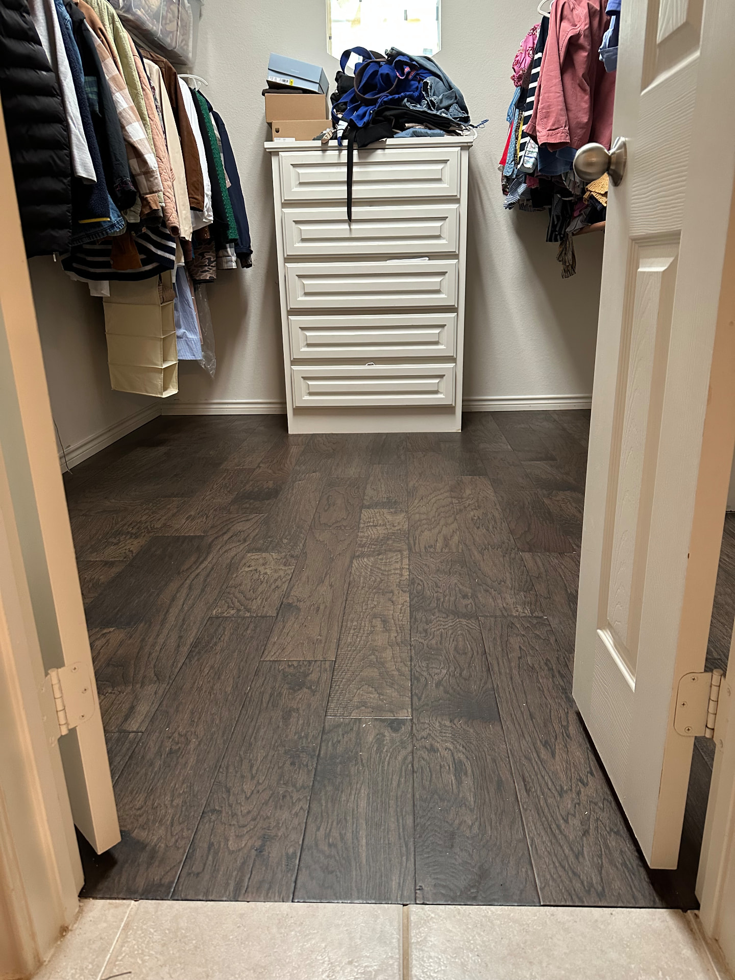 Dark hardwood flooring in a walk-in closet with clothes racks and a white dresser