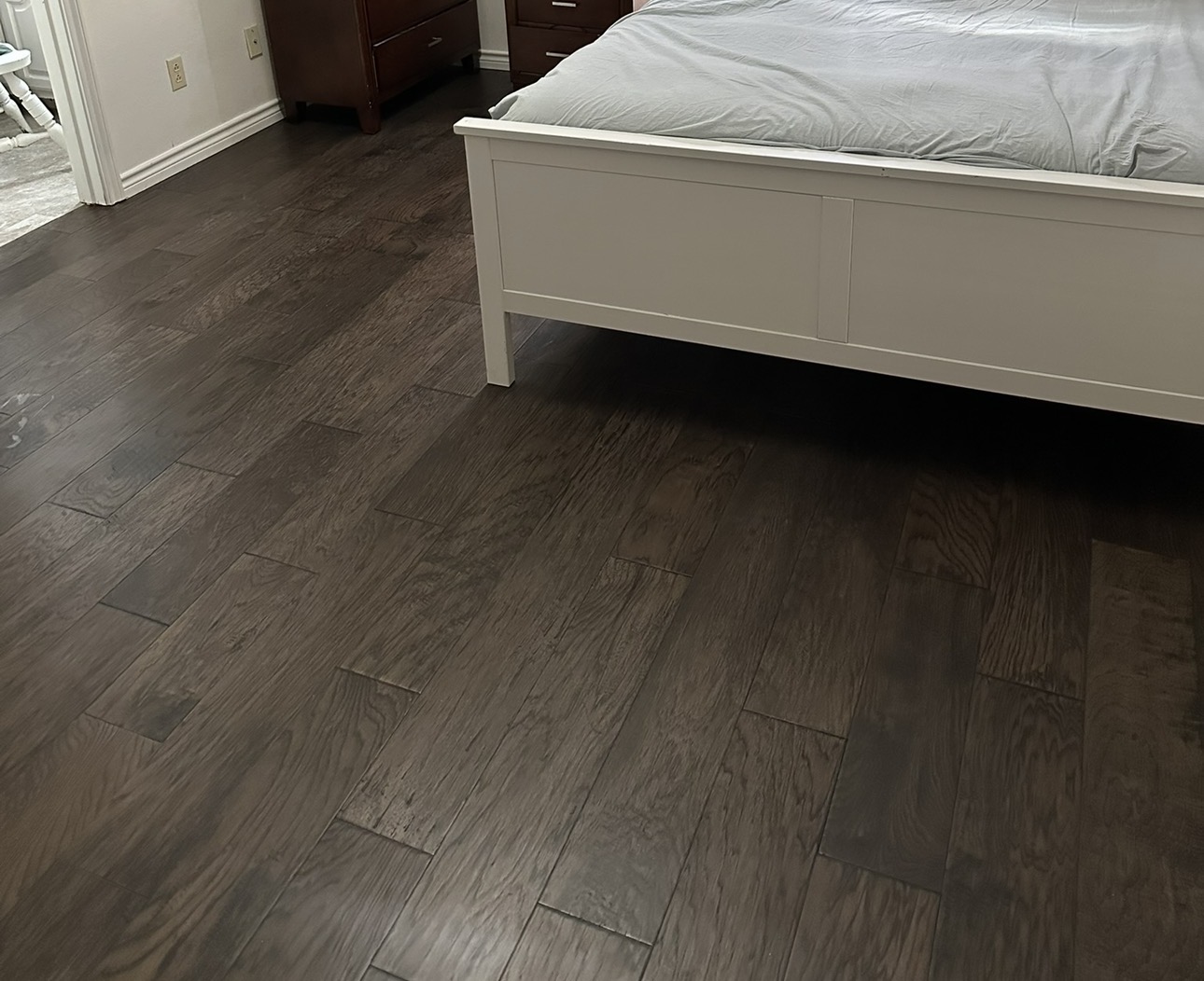 Dark espresso hardwood plank flooring in a bedroom around a white bed frame